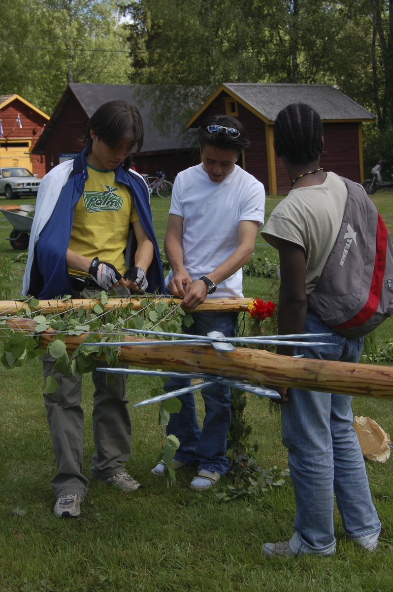 Thumbnail: Ungdomar från Vörå migrationscenter i Oravais ...
	
		Ungdomar från Vörå migrationscenter i Oravais spänner upp streck, tråd med löv, på midsommarstången.