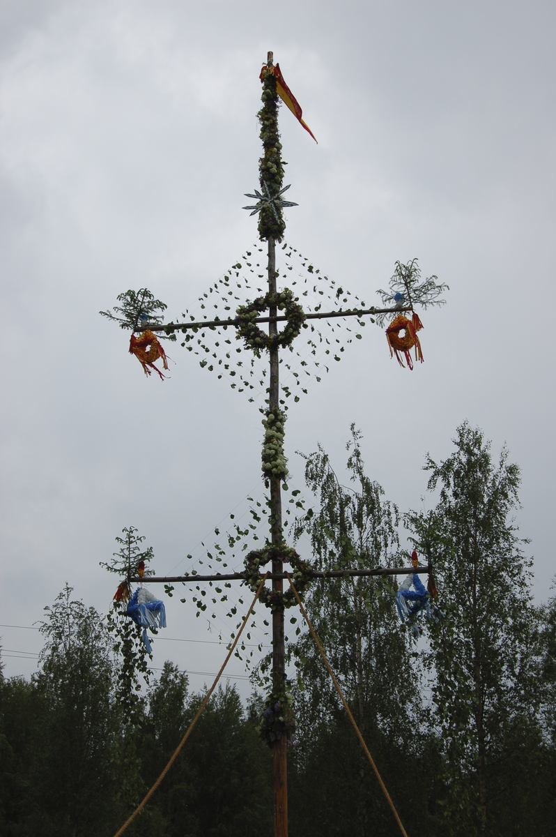 Thumbnail: Midsommarstången är rest mot en regntung himmel.